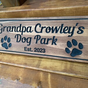 May include: A wooden sign with the text "Grandpa Crowley's Dog Park Est. 2023" and two black paw prints.