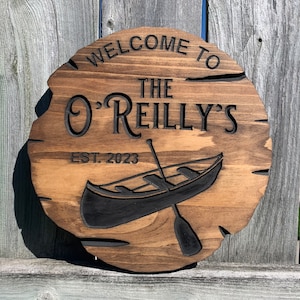 May include: A round wooden sign with the text "Welcome to the O'Reilly's Est. 2023" and a black silhouette of a canoe with a paddle.