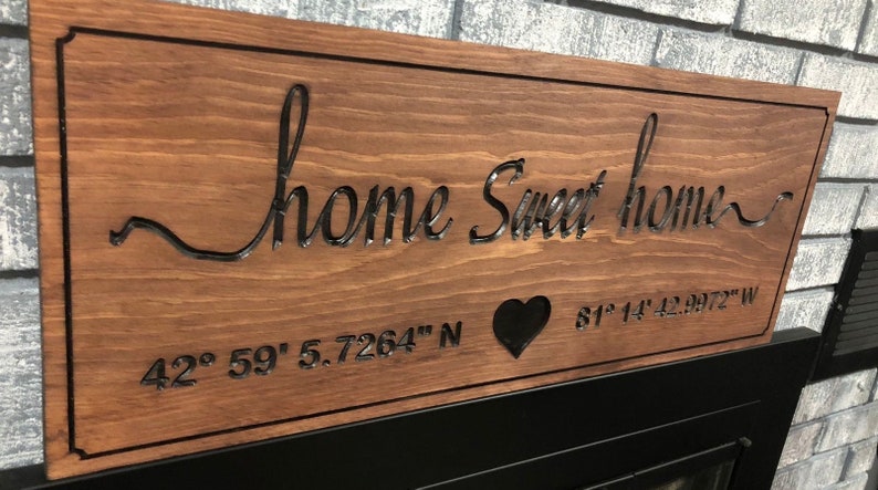 Peut inclure: Panneau en bois marron avec l'inscription "home Sweet home" en lettres cursives. Le panneau comporte un c&oelig;ur et des coordonn&eacute;es g&eacute;ographiques : 42&deg; 59' 5.7264" N et 81&deg; 14' 42.9972" W. Bordure noire.