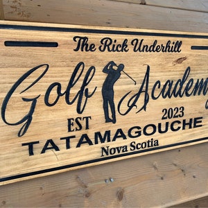 May include: A wooden sign with black lettering that reads "The Rick Underhill Golf Academy Est 2023 Tatamagouche Nova Scotia". The sign features a silhouette of a golfer swinging a club.