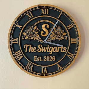 May include: A circular wooden clock featuring Roman numerals and the inscription "The Swigarts Est. 2026." The clock face is black with gold detailing, including a floral pattern and the letter "S."