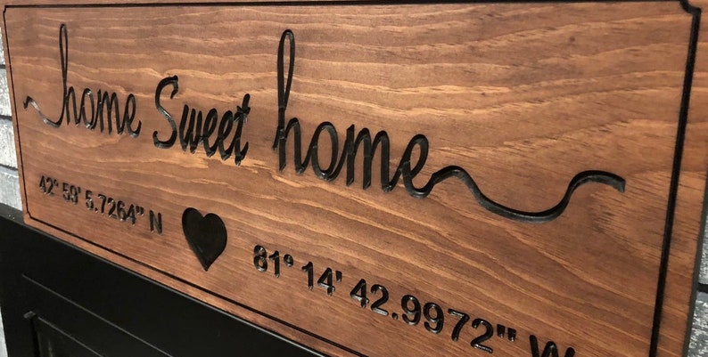Peut inclure: Panneau en bois brun avec l'inscription "home sweet home" grav&eacute;e. Le panneau comprend un symbole de c&oelig;ur et des coordonn&eacute;es. Le texte et le c&oelig;ur sont sombres, cr&eacute;ant un contraste avec le bois.