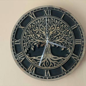 May include: Round wooden wall clock with a tree of life design. The clock face is dark blue with Roman numerals and a light brown tree carving in the center. The clock hands are silver.