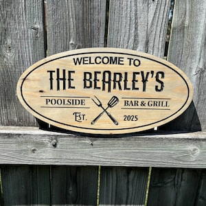 May include: Oval wooden sign with the text "WELCOME TO THE BEARLEY'S POOLSIDE BAR & GRILL EST. 2025". The sign features a crossed fork and spatula design.