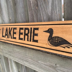 May include: A wooden sign with the words "LAKE ERIE" carved into it. The sign is decorated with two black and white loon illustrations.