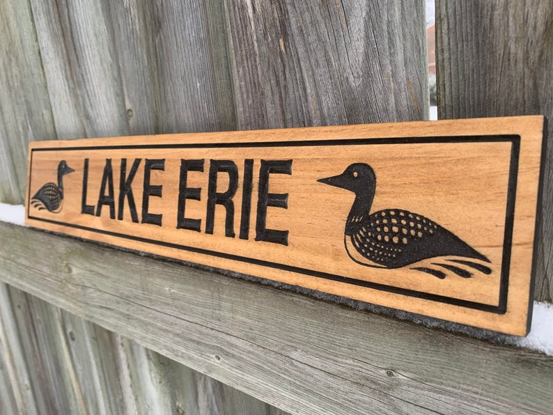 May include: A wooden sign with the words "LAKE ERIE" carved into it. The sign is decorated with two black and white loon illustrations.