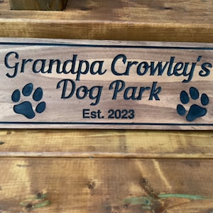 May include: A wooden sign with the text "Grandpa Crowley's Dog Park Est. 2023" and two black paw prints.