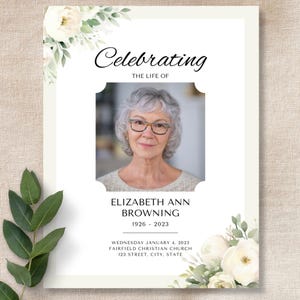 Könnte beinhalten: Eine Trauerprogramm-Vorlage mit einem zentralen Foto einer älteren Person mit grauem Haar und Brille. Der Text lautet Celebrating The Life Of, Elizabeth Ann Browning, 1926-2023, sowie Veranstaltungsdetails, verziert mit weißen Blumenillustrationen.