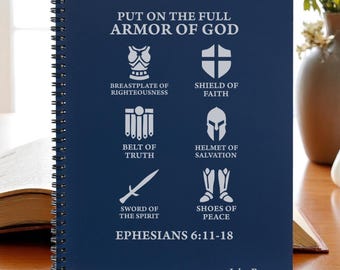 May include: A navy blue spiral-bound notebook with white text and illustrations. The cover displays the phrase "PUT ON THE FULL ARMOR OF GOD" and images of armour. The text "EPHESIANS 6:11-18" is also present, along with the name "John Rogers" at the bottom.