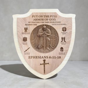 May include: Wooden shield with a light wood border and a central design. The shield features a detailed engraving of a knight, surrounded by text and symbols. The text reads "PUT ON THE FULL ARMOR OF GOD, EPHESIANS 6:11-18".