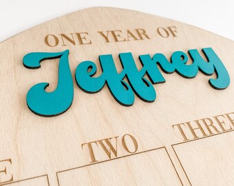 May include: A wooden growth chart with the words "One Year of Jeffrey" in teal lettering. The chart has three sections labeled "One", "Two", and "Three".