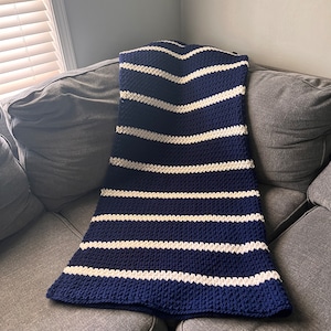 May include: A navy blue and white striped crocheted throw blanket on a gray couch.