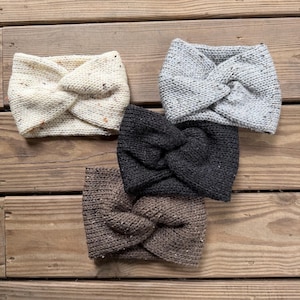 May include: Four knitted headbands in cream, gray, black, and brown, each with a twisted knot design. The headbands are made of a textured yarn and are displayed on a wooden surface.
