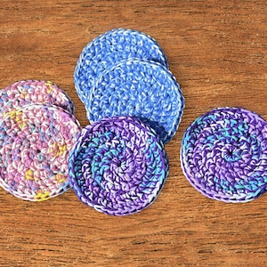 May include: Four crocheted round coasters in blue, purple, and pink with white accents. The coasters are made with a spiral pattern.
