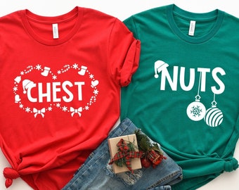 Puede incluir: Dos camisetas rojas y verdes con temática navideña. La camiseta roja dice "Chest" con una corona de Navidad y adornos. La camiseta verde dice "Nuts" con un gorro de Papá Noel y adornos navideños.