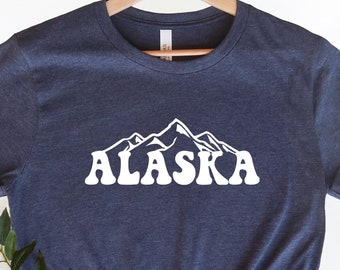 May include: A navy blue t-shirt with a white graphic of mountains and the word "ALASKA" in a retro font.