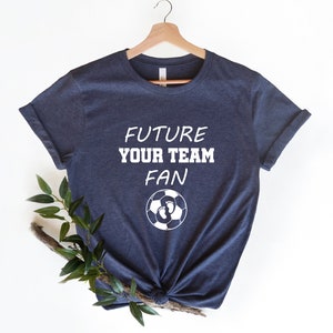 May include: A navy blue t-shirt with white text that reads "Future Your Team Fan" and a soccer ball with footprints inside.