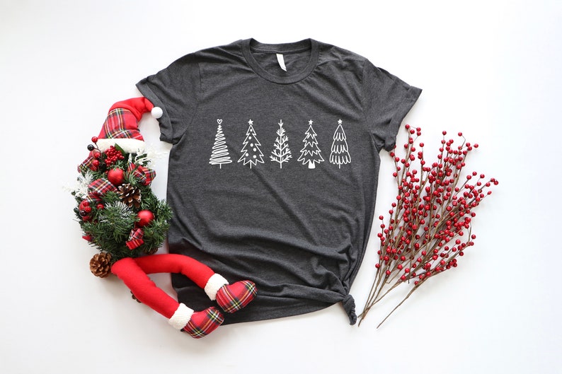 K&ouml;nnte beinhalten: Ein dunkelgraues T-Shirt mit einem wei&szlig;en Design aus f&uuml;nf stilisierten Weihnachtsb&auml;umen. Die B&auml;ume sind in einer Reihe &uuml;ber die Mitte des Shirts angeordnet.