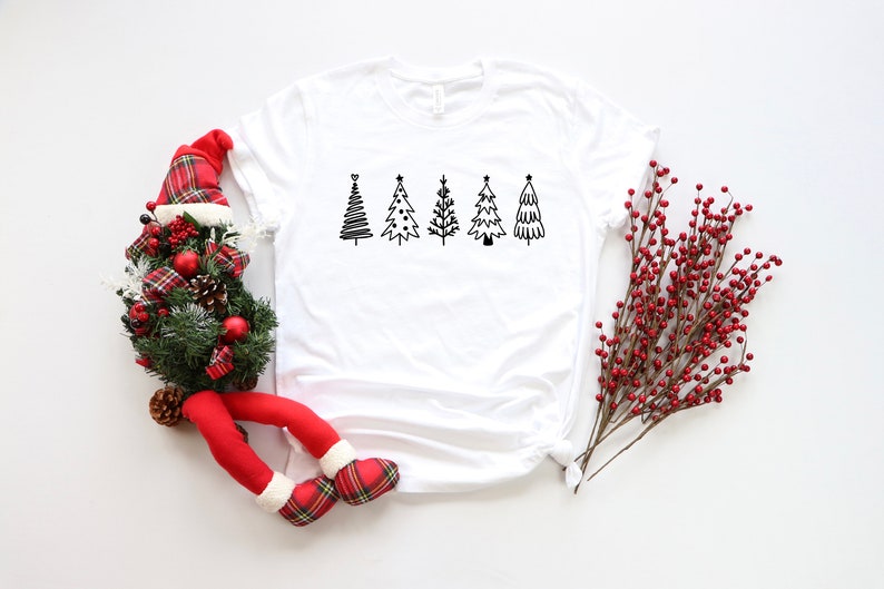 K&ouml;nnte beinhalten: Wei&szlig;es T-Shirt mit einer schwarz-wei&szlig;en Grafik von f&uuml;nf stilisierten Weihnachtsb&auml;umen.
