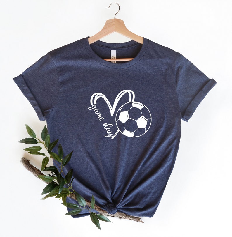May include: A navy blue t-shirt with a white graphic of a soccer ball and the text "game day" in a heart shape.
