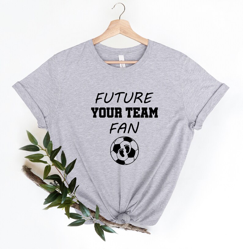 May include: Gray t-shirt with the text "FUTURE YOUR TEAM FAN" and a soccer ball with baby footprints on it.
