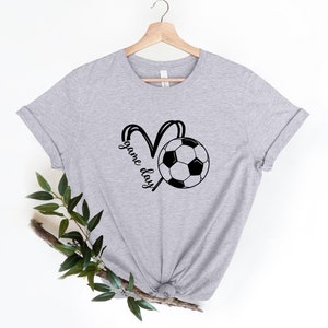 May include: Gray t-shirt with a black and white soccer ball graphic and the text "game day" in a heart shape.