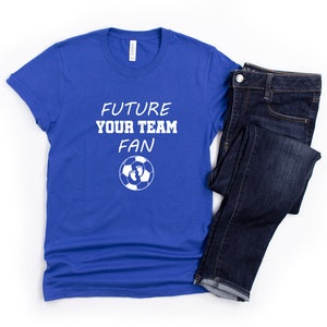 May include: A royal blue t-shirt with white text that reads "Future Your Team Fan" and a soccer ball with footprints on it.