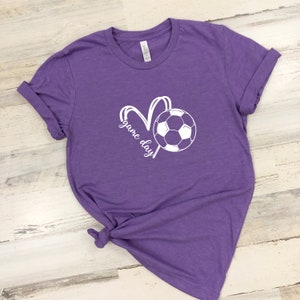 May include: Purple t-shirt with a white soccer ball and the text "game day" in a heart shape.