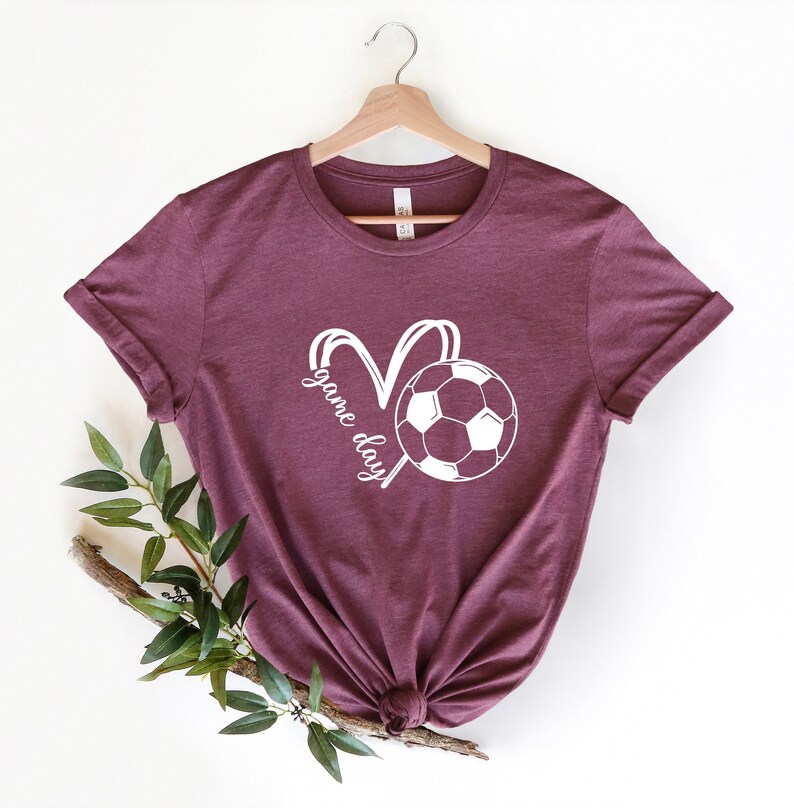 May include: Burgundy t-shirt with a white soccer ball and the text "game day" in a heart shape.