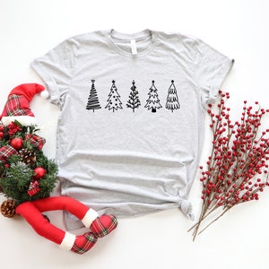 K&ouml;nnte beinhalten: Ein graues T-Shirt mit einer Reihe von f&uuml;nf schwarzen und wei&szlig;en Weihnachtsbaum-Illustrationen.
