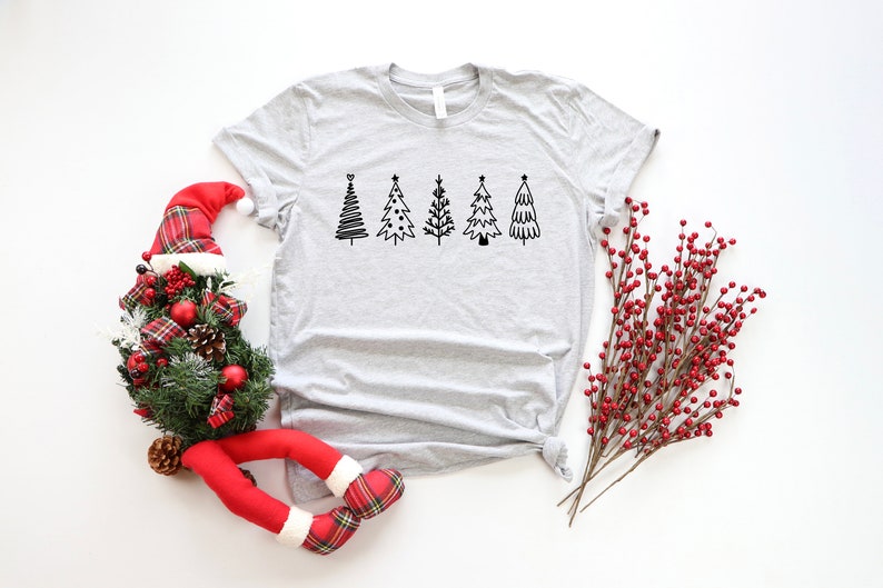 K&ouml;nnte beinhalten: Ein graues T-Shirt mit einer Reihe von f&uuml;nf schwarzen und wei&szlig;en Weihnachtsbaum-Illustrationen.