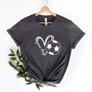 May include: A dark gray t-shirt with a white soccer ball and the words "game day" in a heart shape.