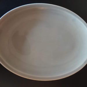 Puede incluir: Una fuente ovalada de cerámica gris claro. La fuente tiene una superficie lisa y un borde ligeramente elevado. El color neutro y el diseño sencillo la hacen adecuada para diversas presentaciones culinarias.