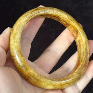 May include: A circular bangle bracelet with a smooth, polished surface. The bracelet features a mottled, translucent golden-yellow and brown colour palette with visible natural grain patterns throughout the material, creating a unique appearance.