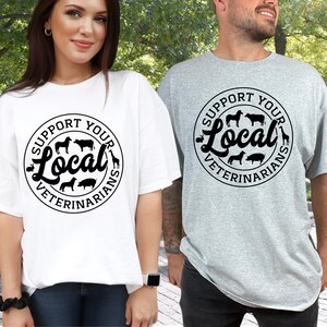 May include: Two people wearing t-shirts with a black and white graphic design. The graphic says "Support Your Local Veterinarians" with a circle around the text and images of farm animals inside the circle.