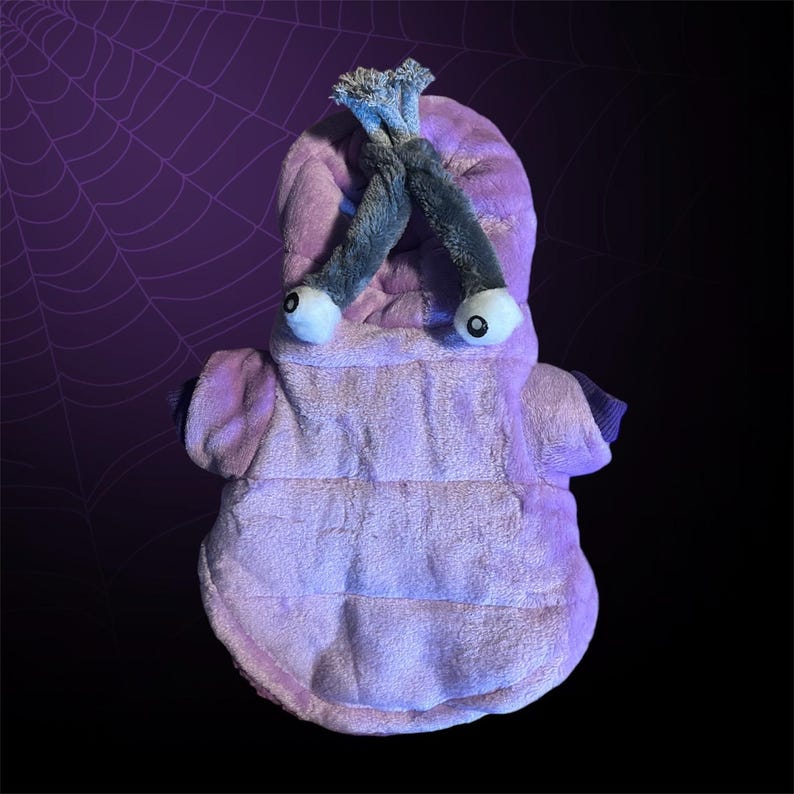 May include: Purple plush dog costume with a hooded head shaped like a monster with two large eyes and a long, curled tail.