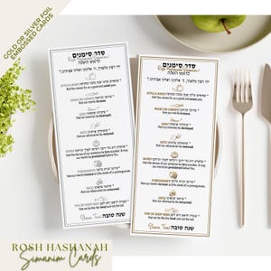 May include: Two rectangular Rosh Hashanah Simanim cards featuring Hebrew and English text with illustrations of symbolic foods. One card has silver foil accents, and the other has gold foil accents. The cards list traditional blessings for the holiday.