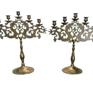 May include: Pair of antique brass candelabras. Each candelabra features a decorative dragon design and holds five candle holders. The candelabras have a round base and a detailed stem. The overall color is a warm brass tone.