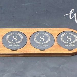 Puede incluir: Una bandeja de servir de madera con cuatro posavasos redondos de pizarra. Cada posavasos tiene una inicial "S" dorada y el texto "The Shelton" grabado. La bandeja tiene un asa y el texto "SUPREME Whiskey STONES" está impreso en la parte superior.