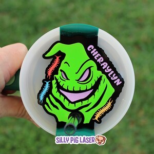 Puede incluir: Un personaje verde y negro con una sonrisa de dientes y una lengua rosa, con el nombre "CHERYAYLYN" escrito en blanco sobre un fondo negro. El personaje est&aacute; rodeado de formas coloridas en forma de gusano. La imagen est&aacute; sobre un fondo blanco con un borde verde.