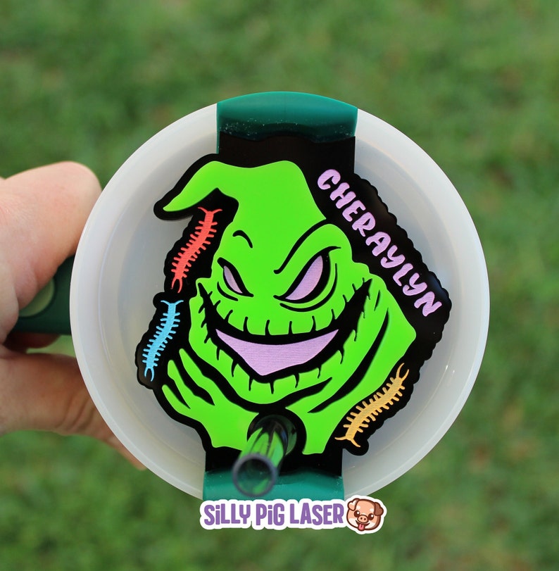 Puede incluir: Un personaje verde y negro con una sonrisa de dientes y una lengua rosa, con el nombre "CHERYAYLYN" escrito en blanco sobre un fondo negro. El personaje est&aacute; rodeado de formas coloridas en forma de gusano. La imagen est&aacute; sobre un fondo blanco con un borde verde.