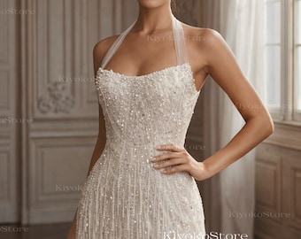 May include: A white, beaded halter-neck wedding dress. The short dress features a fitted bodice and a skirt with beaded fringe. The dress is embellished with numerous small beads, creating a shimmering effect. The text "KiyokoStore Custom wedding dress" is visible.