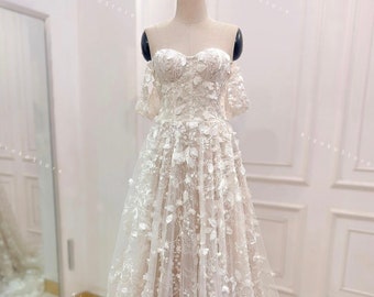 May include: A white off-the-shoulder gown with a fitted bodice and a flowing skirt. The gown is covered in delicate floral embroidery.