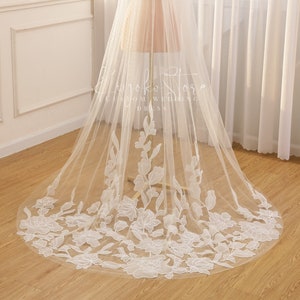 Può includere: Un velo da sposa bianco con ricami floreali delicati. Il velo è realizzato in tulle morbido e ha un lungo strascico fluido.