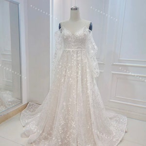 May include: A white off-the-shoulder wedding dress with a sweetheart neckline and a tulle skirt. The dress is covered in small white stars.