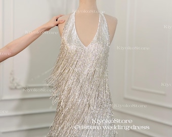 May include: A silver, fringed halter dress with a deep V-neck, displayed on a mannequin. A gold crown sits atop the mannequin's head. The dress is labeled "Custom wedding dress".