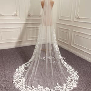 May include: A white bridal veil with delicate floral lace trim. The veil is long and flowing, with a soft, sheer fabric.