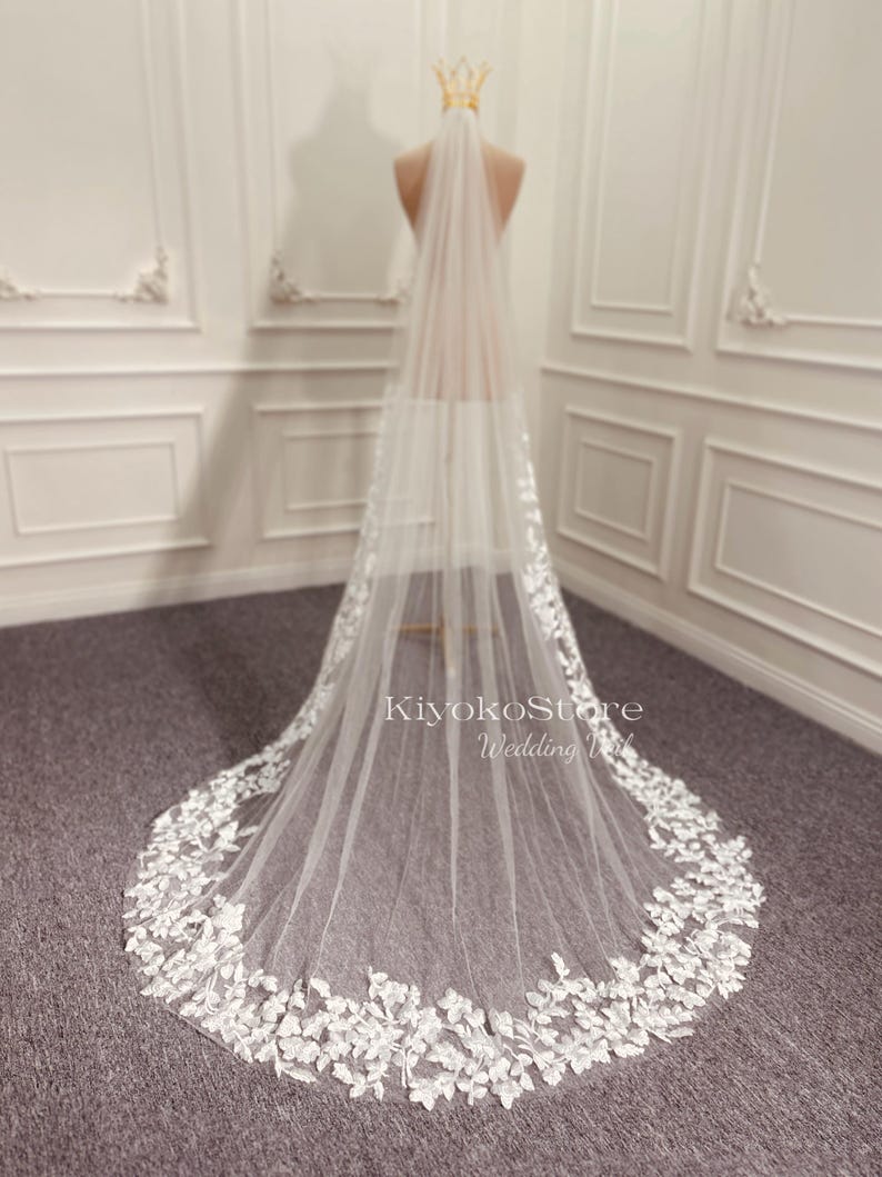 May include: A white bridal veil with delicate floral lace trim. The veil is long and flowing, with a soft, sheer fabric.