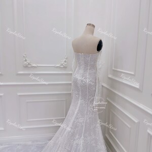 May include: A white wedding dress with a fitted bodice and a flowing skirt. The dress is covered in delicate lace and beading. The dress has a sweetheart neckline and a long train.
