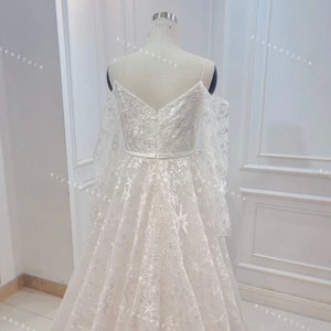 May include: A white wedding dress with a sweetheart neckline and a tulle skirt. The dress features a star-shaped pattern and a sheer overlay. The dress is shown from the back.